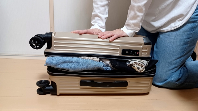 スーツケースに荷物を押し込む男性